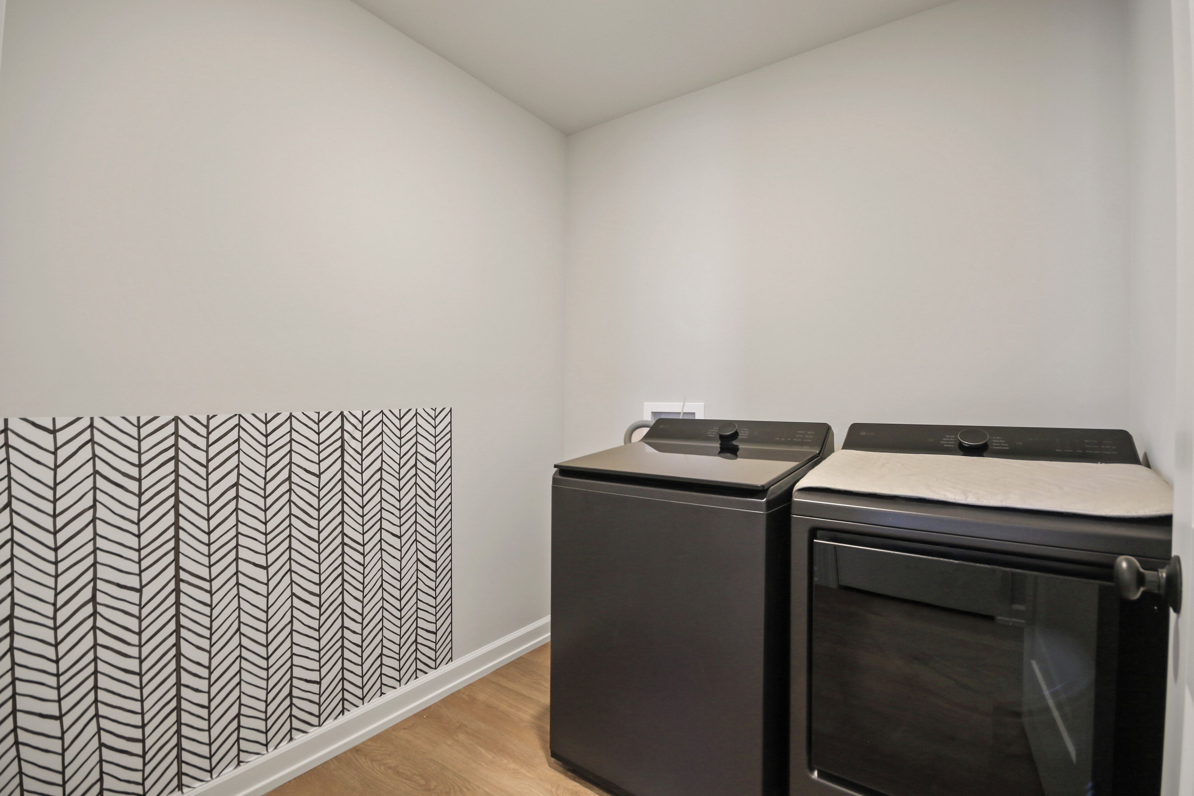 A laundry room with a washing machine and dryer, a patterned wall, and a wooden floor.