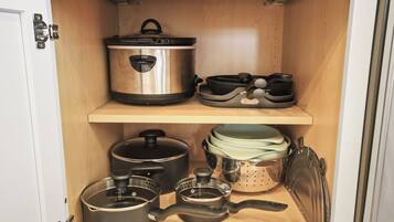 A kitchen cabinet with stainless steel cookware, including pots, pans, and a colander.