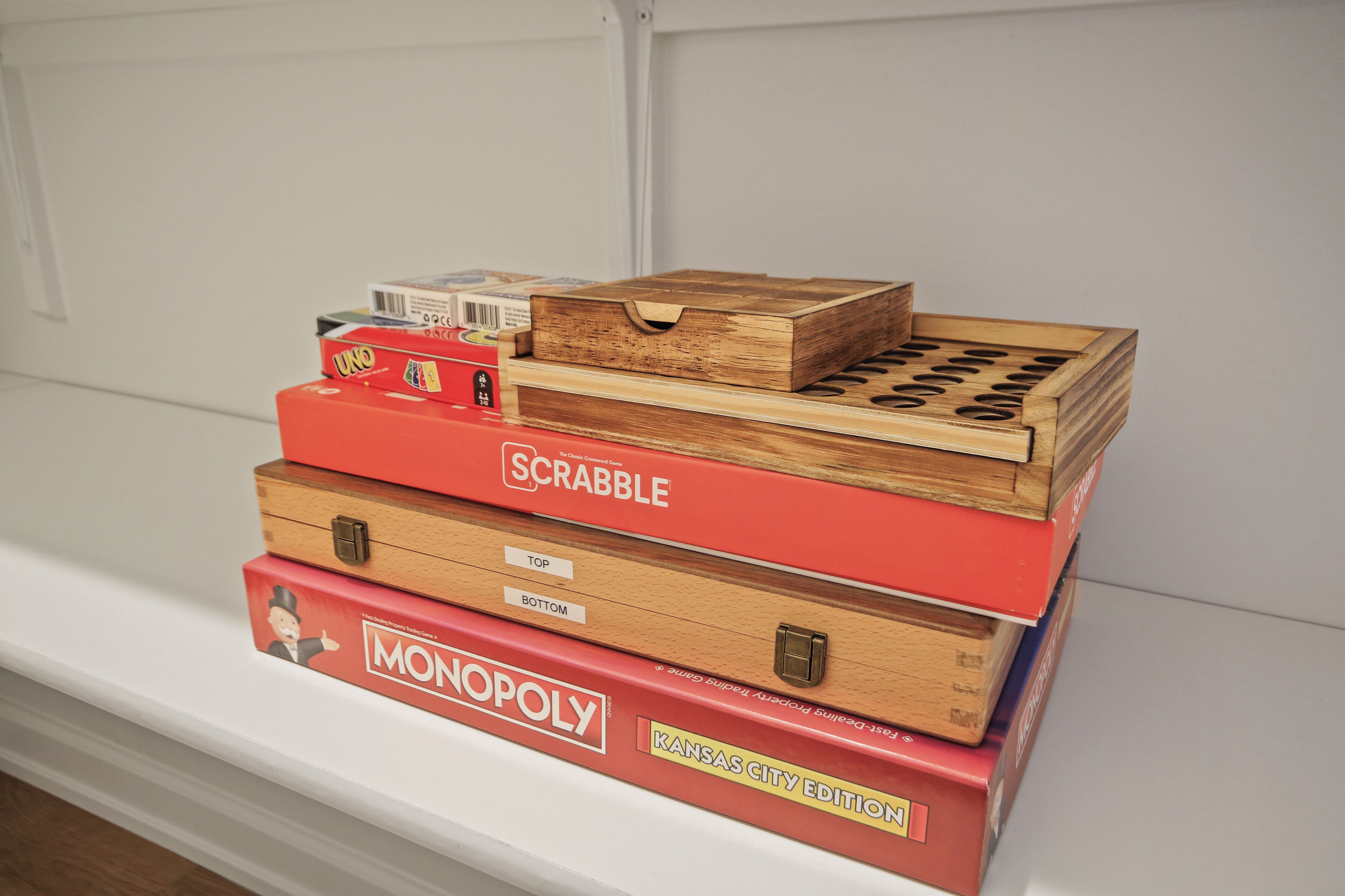 Une pile de jeux de société, dont UNO, Scrabble et Monopoly, est posée sur une étagère.
