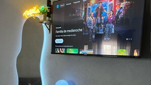 Un televisor de pantalla plana montado en la pared mostrando un programa titulado 'Familia de medianoche'.