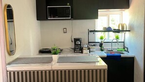 Cocina compacta con microondas, cafetera y un lavamanos pequeño.