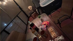 Un área de comedor con una mesa dispuesta para dos personas, que incluye una botella de Coca-Cola, dos vasos, un plato de aperitivos y un recipiente de plástico con galletas.