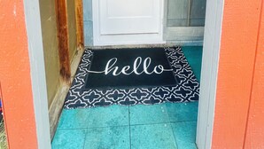 Un acceso estrecho con una puerta blanca, un felpudo estampado y un suelo verde azulado.