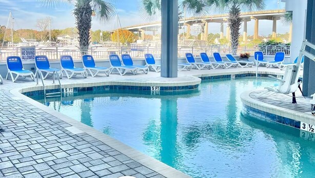 An indoor swimming pool with clear water, surrounded by blue lounge chairs and palm trees.