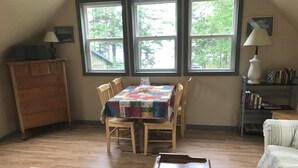 Un comedor con una mesa y sillas de madera, un mantel acolchado y vistas a través de amplios ventanales.