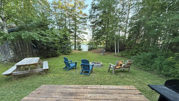 Un espacio de estar al aire libre rústico con una mesa de picnic de madera, dos sillas Adirondack y un brasero.