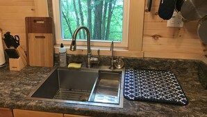 Una cocina con un lavamanos doble, una ventana con vistas a árboles y un colgador para ollas.