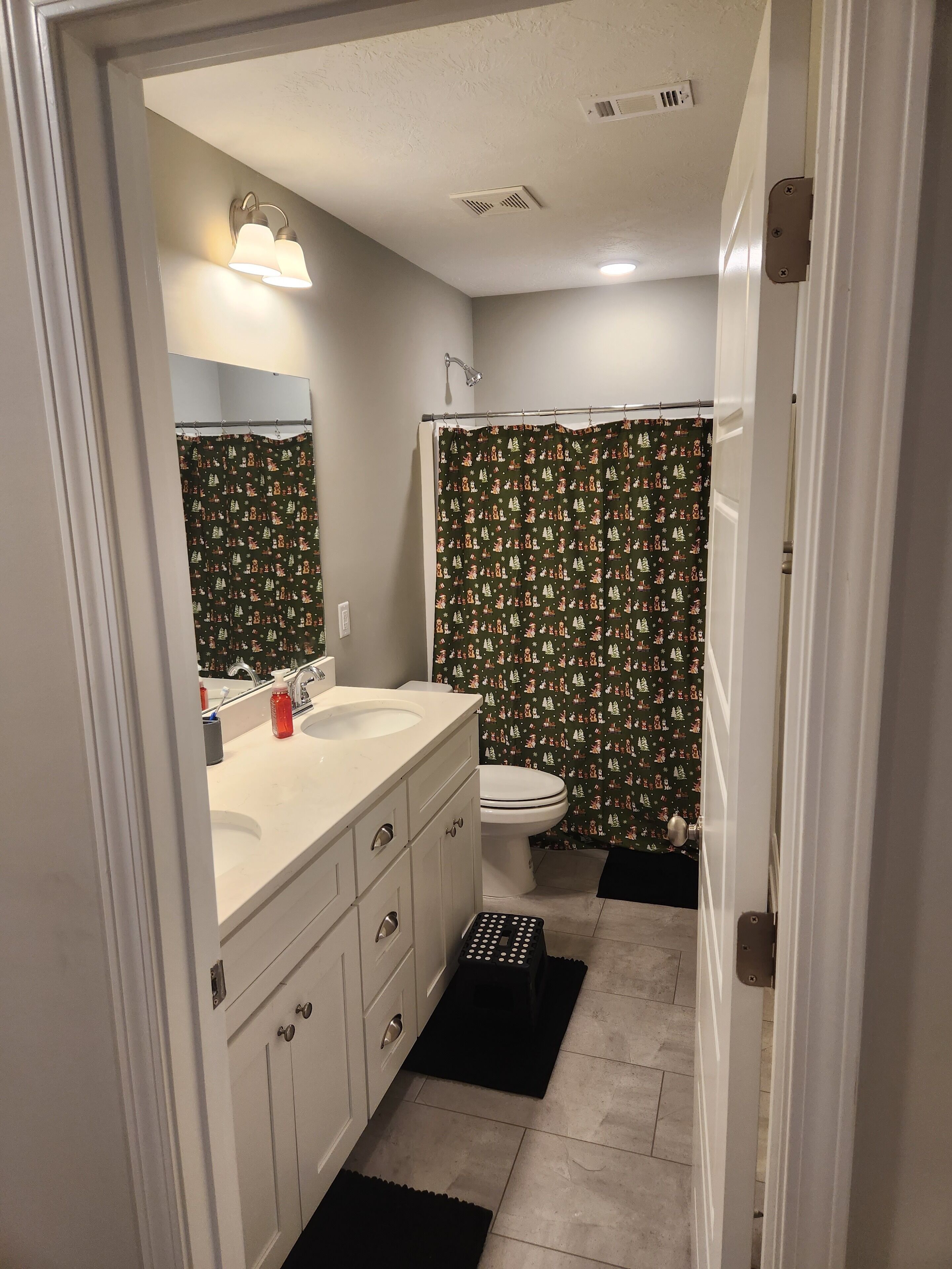 A bathroom with a white sink, mirror, and toilet. There is a shower curtain with a Christmas pattern.