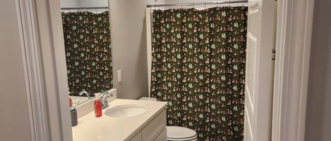 A bathroom with a white sink, mirror, and toilet. There is a shower curtain with a Christmas pattern.