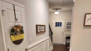 A hallway with a wooden floor, white walls, a door with a hanging decoration, and a staircase leading to another room. - Charming house just minutes to the Augusta National in fabulous North Augusta (North Augusta)