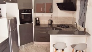 A modern kitchen with a built-in oven, a gas stove, and a microwave. There are two bar stools and a sink. - Villa tempÔ In a quiet, secure residence. Close to the beach and port (Sainte-Rose)