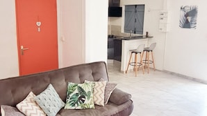 A spacious living area with a grey sofa, red rug, and a kitchen in the background. - Villa tempÔ In a quiet, secure residence. Close to the beach and port (Sainte-Rose)