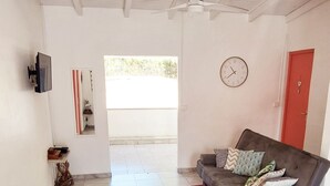 A spacious living room with a grey sofa, a red rug, and a ceiling fan. - Villa tempÔ In a quiet, secure residence. Close to the beach and port (Sainte-Rose)