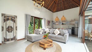 A spacious living area with a grey sofa, a wooden coffee table, and a large window with curtains. - Elephant Villa 5 by Villa Finder (Ubud)