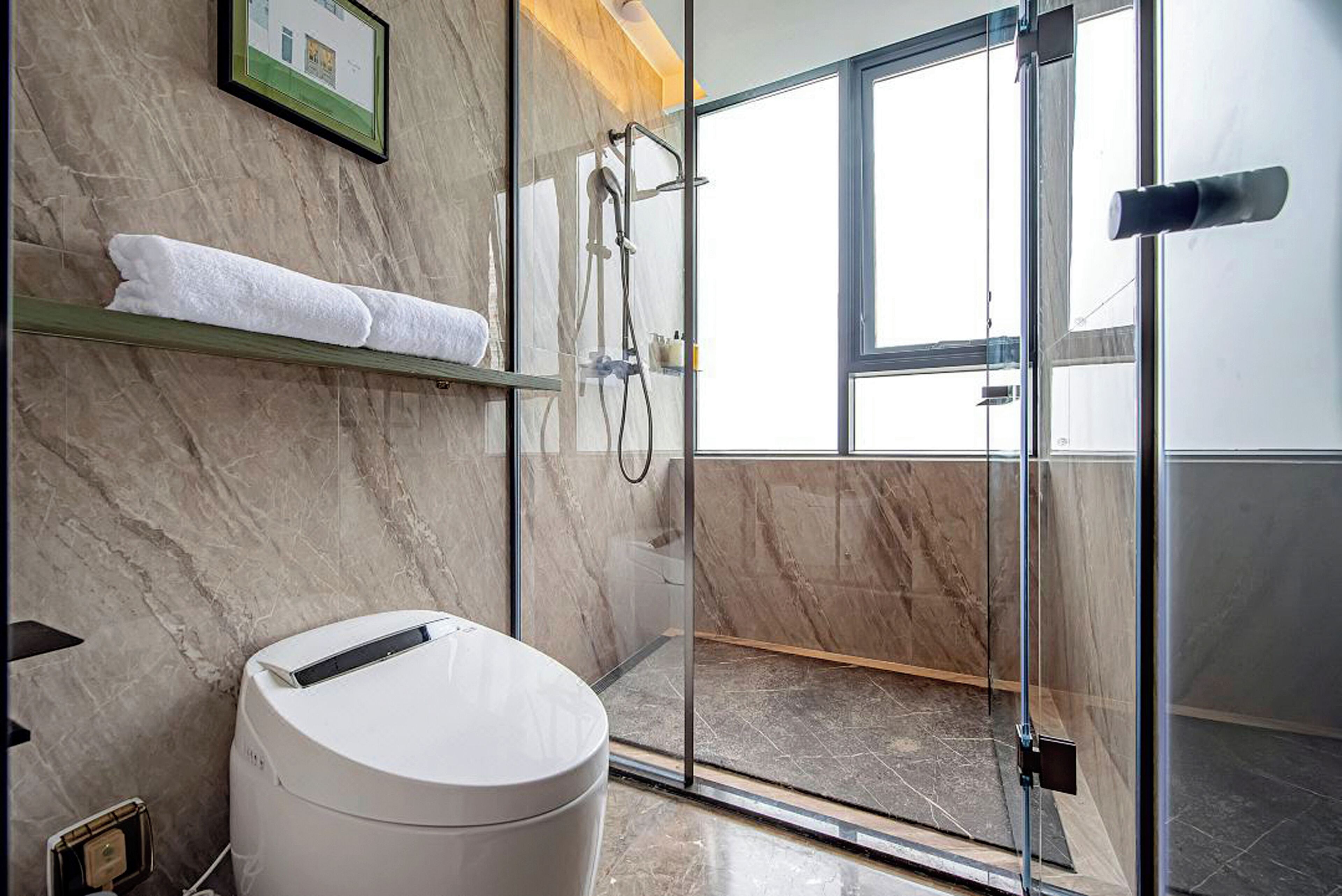 A modern bathroom with a marble floor, a glass shower enclosure, and a toilet with a white lid.