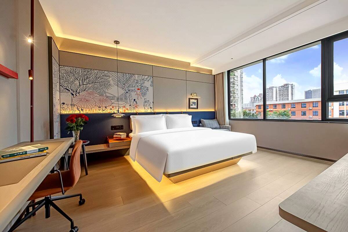 A modern hotel room with a large bed, a desk, and a city view.
