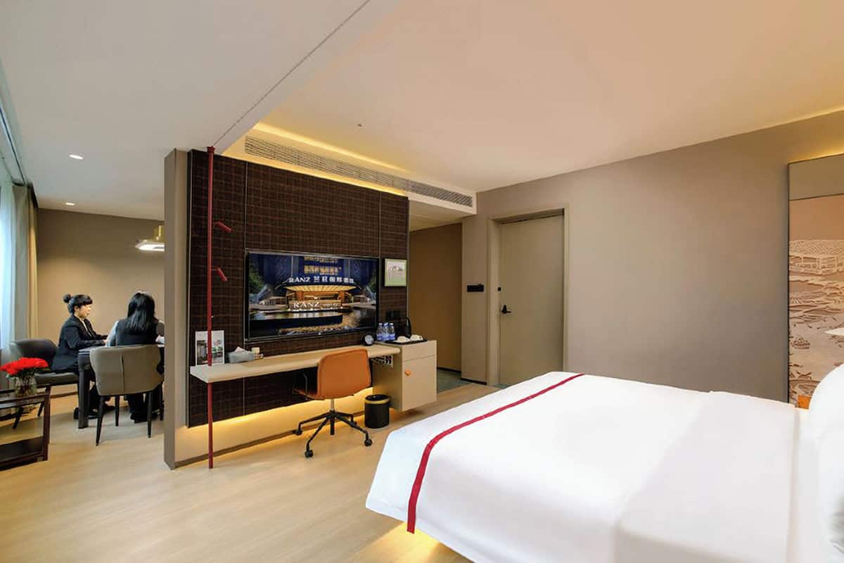 A hotel room with a bed, a desk, a TV, and a seating area with two chairs.