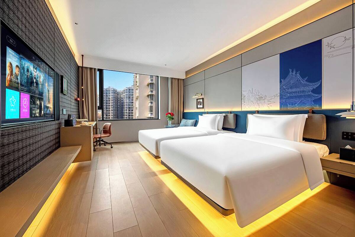 A modern hotel room with a large bed, a desk, and a TV displaying movie posters.
