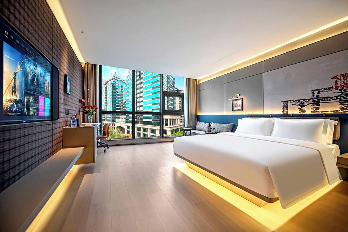 A modern hotel room with a large bed, a desk, and a TV mounted on the wall.