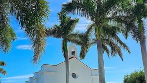 Ein weißes Gebäude mit einem Glockenturm, umgeben von Palmen und Kies.