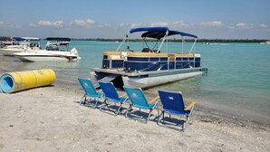 Ein Strand mit einem schwebenden Boot, einem gelben Fass und blauen Liegestühlen.