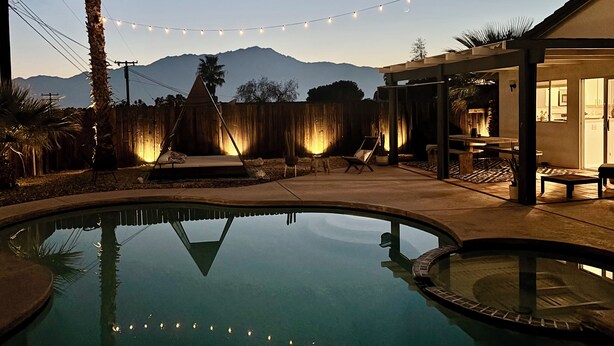 A backyard with a swimming pool, a wooden deck, and string lights. - Charming 3-bedroom house with Pool/Jacuzzi and Desert Mountain View (Desert Hot Springs)