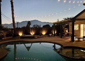 A backyard with a swimming pool, a wooden deck, and string lights. - Charming 3-bedroom house with Pool/Jacuzzi and Desert Mountain View (Desert Hot Springs)