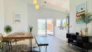 A spacious living area with a wooden dining table, a bench, and a large rug. There is a television on a wooden stand and a plant on the right side. - Charming 3-bedroom house with Pool/Jacuzzi and Desert Mountain View (Desert Hot Springs)