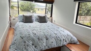 A bedroom with a bed, a bench, and a window. - Luxury Beach Bus (Whanganui)