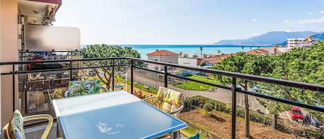 A balcony with a table and chairs, overlooking a coastal area with buildings and greenery.