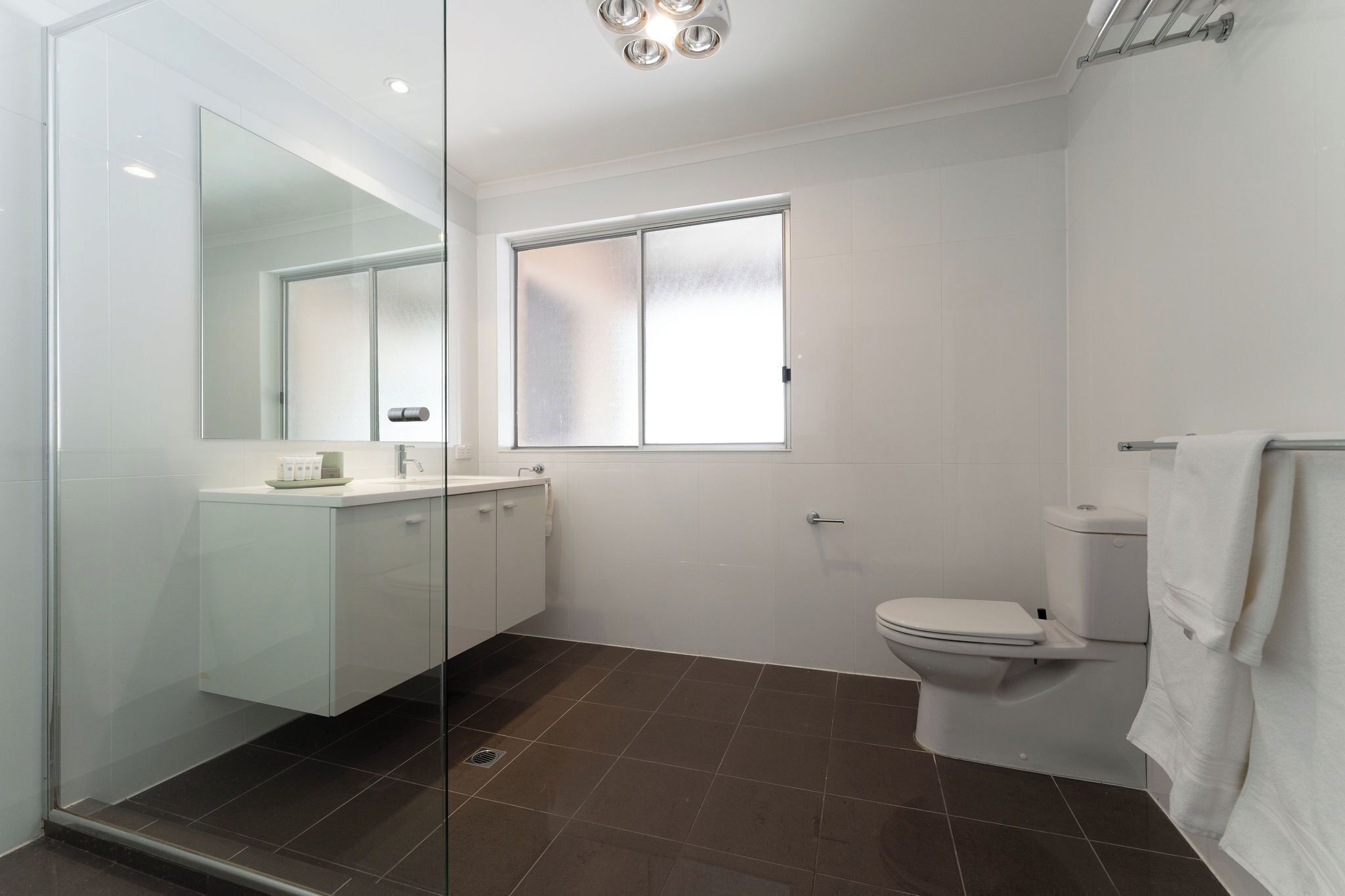 Un baño moderno con cabina de ducha de vidrio, inodoro blanco y ventana que proporciona luz natural.