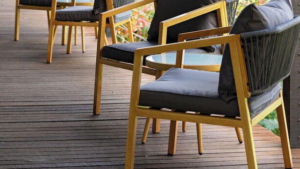 A covered outdoor seating area with wooden chairs and cushions, overlooking a garden. - Mount Lofty Golf Course (Stirling)