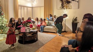 Un salon décoré d’un sapin de Noël, une table basse sur laquelle sont posés des cadeaux, et un groupe de personnes assises sur un canapé.