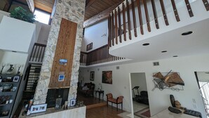 Un intérieur spacieux avec un plafond haut, un pilier en pierre, des poutres en bois et un escalier menant à un niveau supérieur.