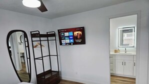 Un dormitorio con cama, televisor en la pared mostrando servicios de streaming, armario de madera y baño con ventana.