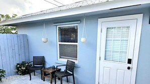 Un patio con una mesa, sillas, una puerta y una ventana con persianas.