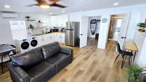Cocina moderna con armarios blancos, refrigerador de acero inoxidable y una zona de comedor con sofá de cuero y mesa de madera.