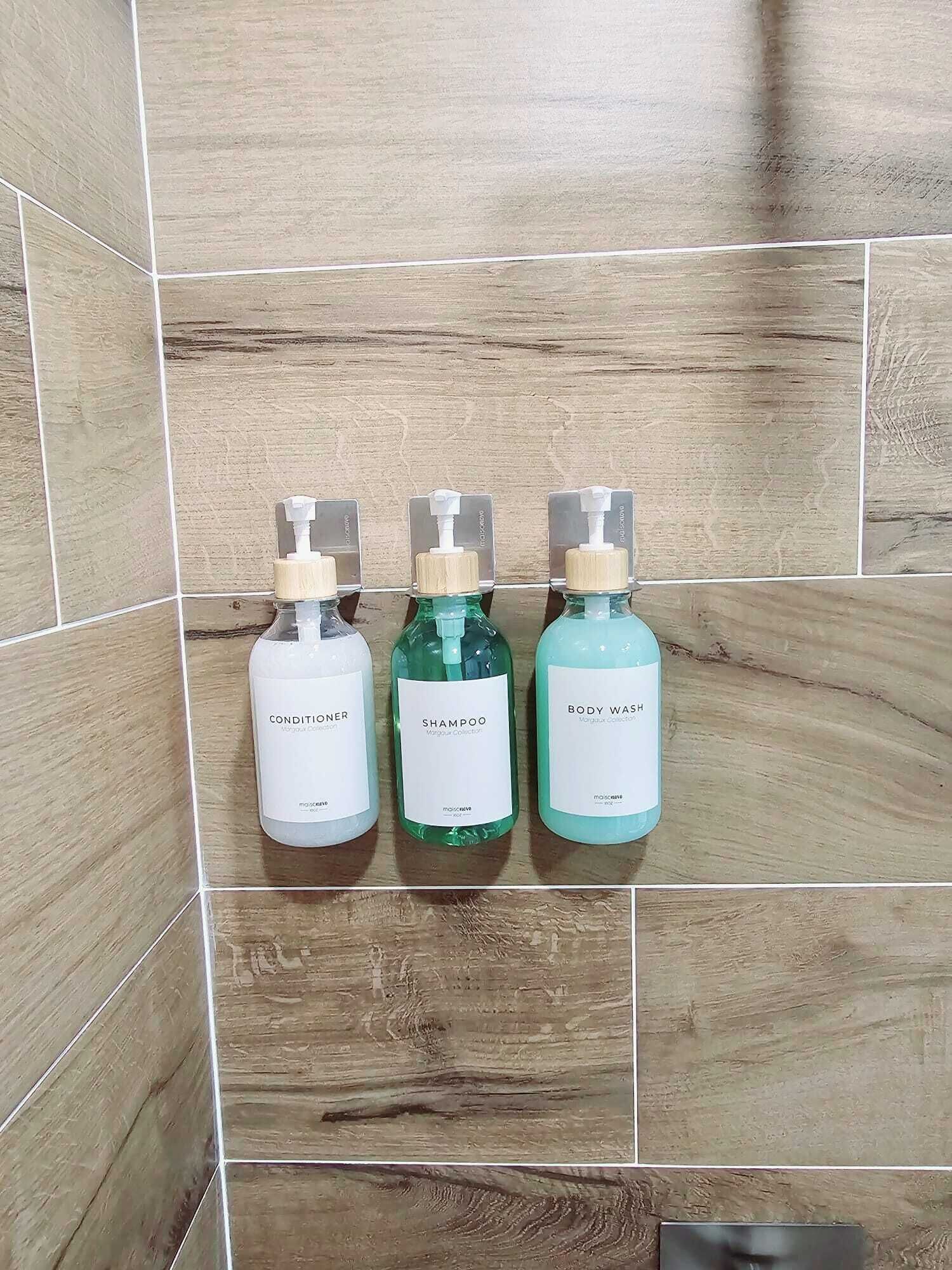 Tres botellas de artículos de aseo sobre una pared de azulejos.