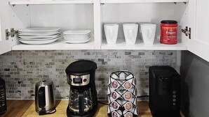 Una cocina con armarios blancos, cafetera, tetera y soporte para cápsulas de café.