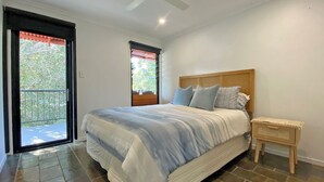 Ein Schlafzimmer mit einem Bett, einem Deckenventilator, einem Fenster mit Blick ins Grüne und einer Balkontür.