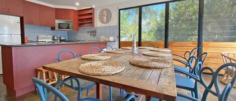 Una cocina moderna con armarios rojos, un microondas y un comedor con una mesa de madera y sillas azules.