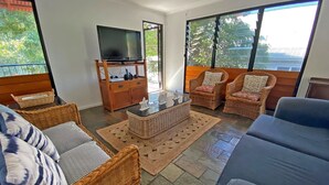 Ein Wohnzimmer mit Rattanmöbeln, einem Fernseher und großen Fenstern.