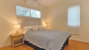 A bedroom with a bed, nightstands, a window with blinds, and an air conditioning unit.