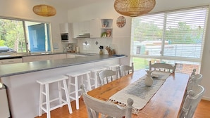 A modern kitchen with white cabinetry, a large island with bar stools, and a dining table with chairs.