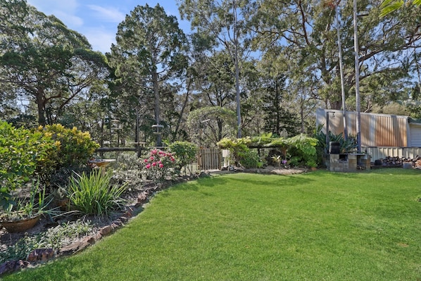 Un jardín bien cuidado con una variedad de plantas y árboles, un césped despejado y una valla de madera.