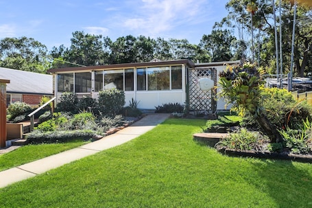 A house with a covered patio, a well-maintained lawn, and a variety of plants.. Original house, large gardens in bush setting