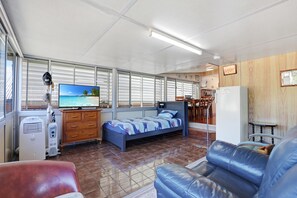 A compact room with a bed, a television, a refrigerator, and a dining area.