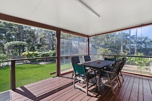 Un espacio al aire libre cubierto con una mesa y sillas, vistas a un jardín cuidado y una terraza de madera.