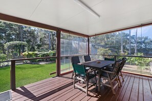 Un espacio al aire libre cubierto con una mesa y sillas, vistas a un jardín cuidado y una terraza de madera.