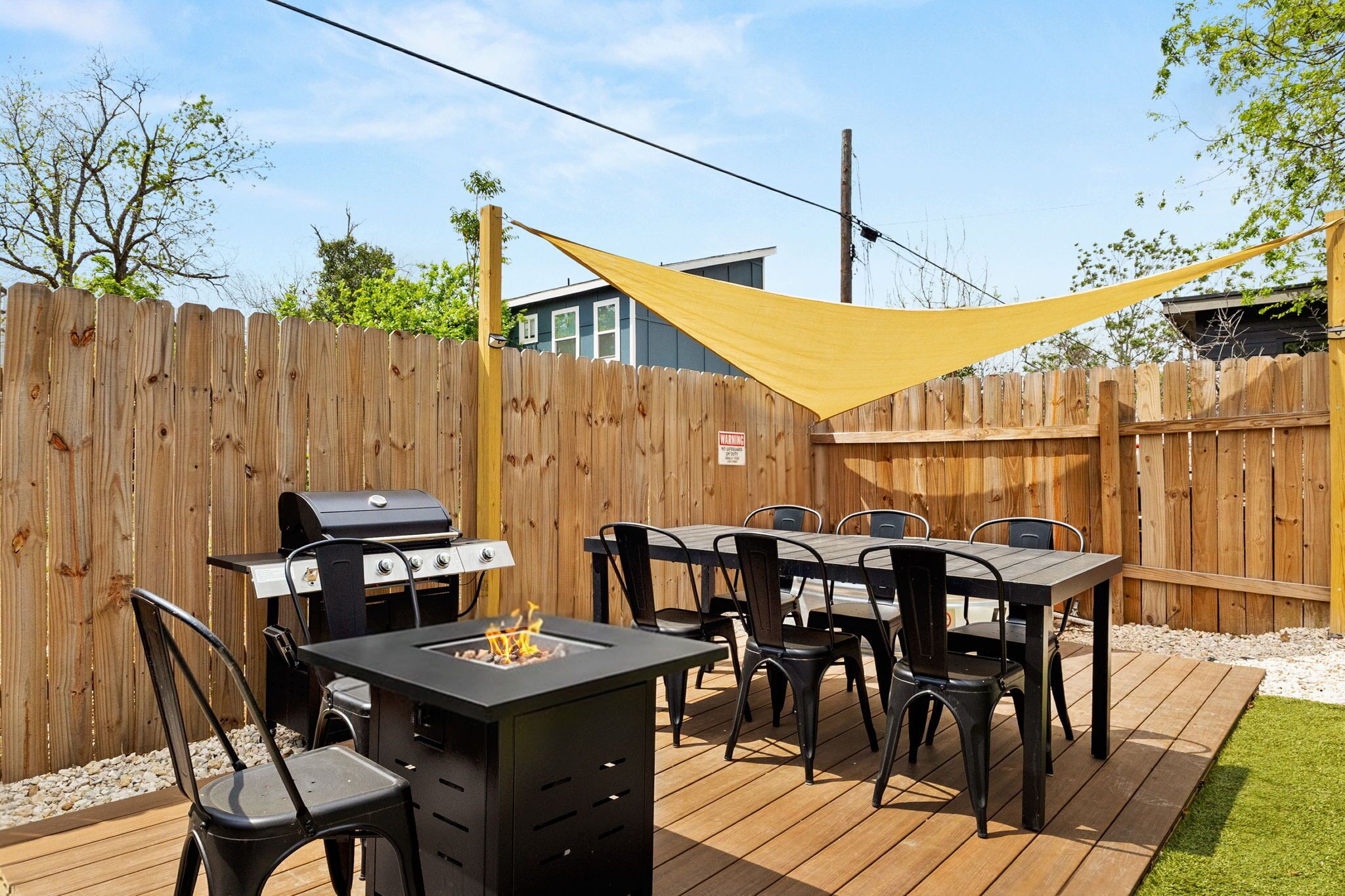 Una terraza de madera con una parrilla, mesa y sillas, una sombrilla amarilla y una cerca de madera.